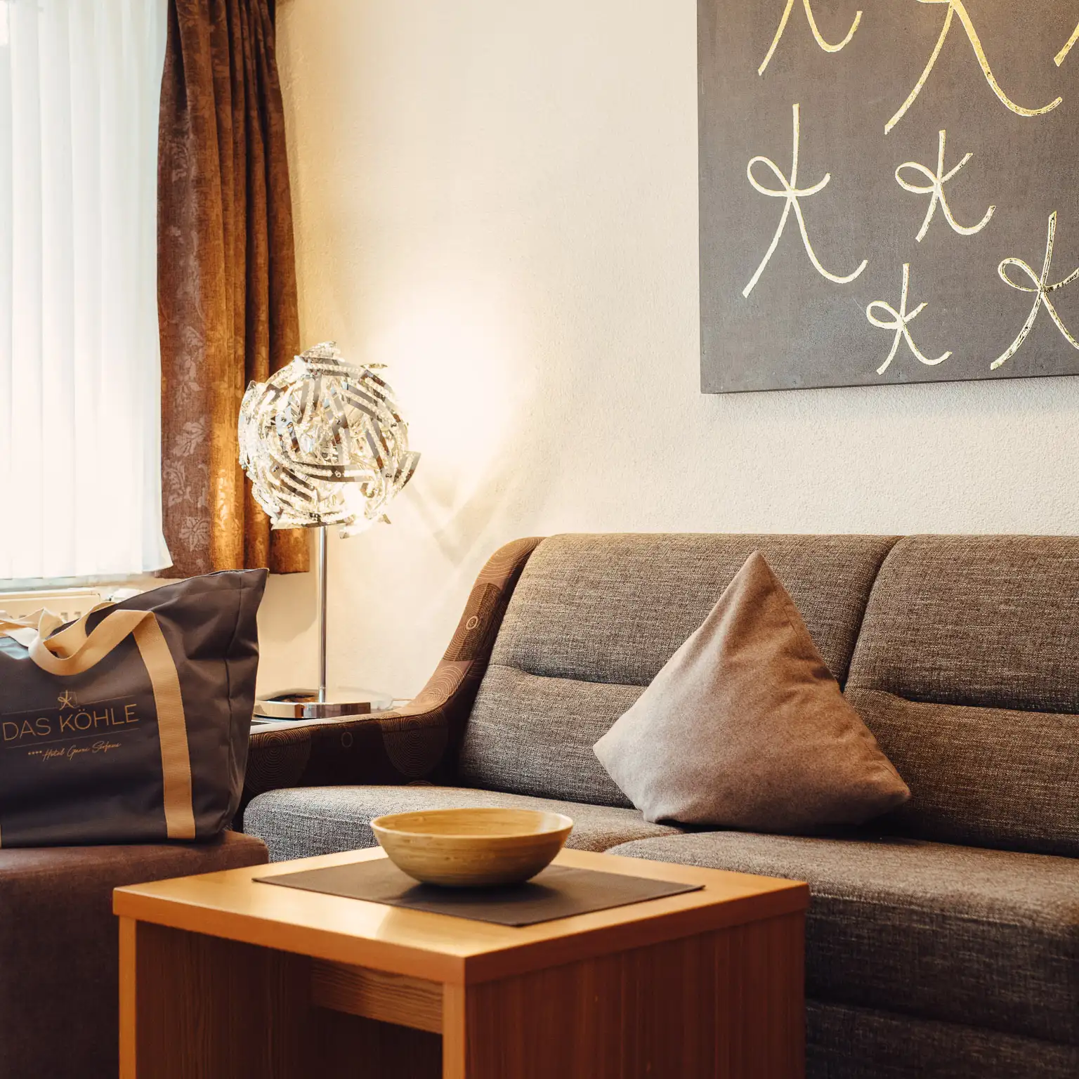 Modernes Wohnzimmer mit grauem Sofa, Holztisch, Lampe und abstrakter Wandmalerei.