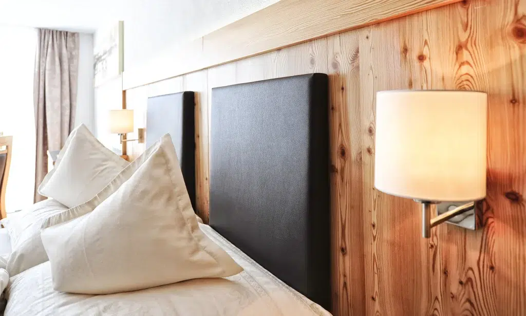Zwei Betten mit weißen Kissen, Lampen an einer Holzwand und ein helles, von Nachhaltigkeit geprägtes Zimmer.