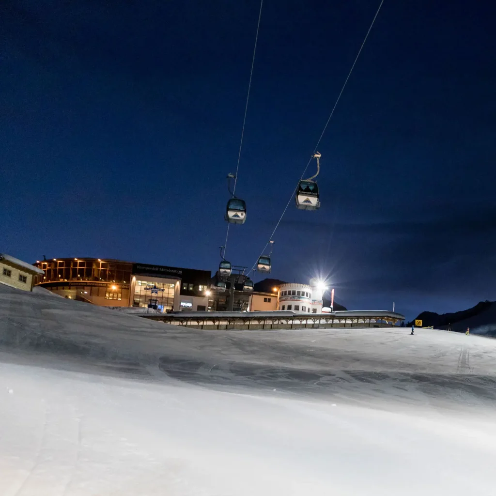 Skigondeln gleiten über eine verschneite Piste, während Nachtskilauf und Nachtrodeln die Nacht erhellen.