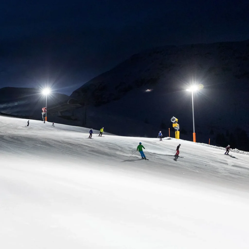 Skifahrer genießen den Nachtskilauf, bei dem sie unter Flutlicht auf einer verschneiten Nachtpiste talwärts fahren.