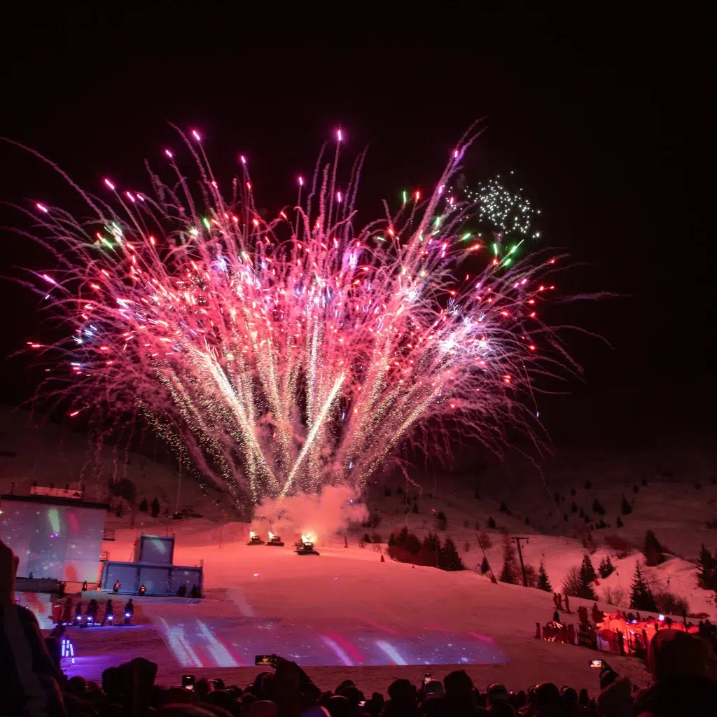 Ein helles Feuerwerk explodiert über einem nächtlichen Schneehang und beleuchtet den darunter liegenden Nightflow.