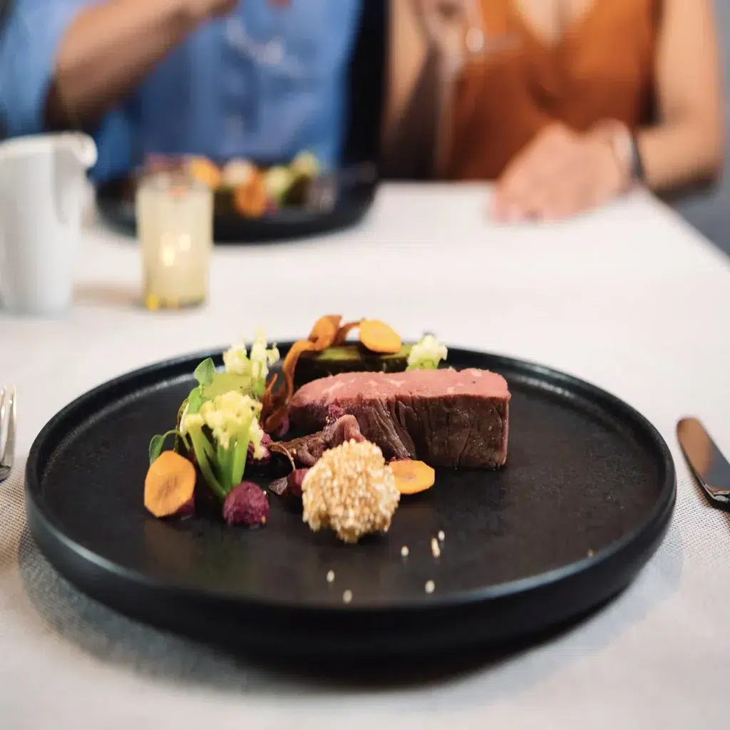 Ein Gourmet-Steakgericht von Das Köhle mit Gemüse auf einem schwarzen Teller, serviert auf einem weißen Tischtuch.