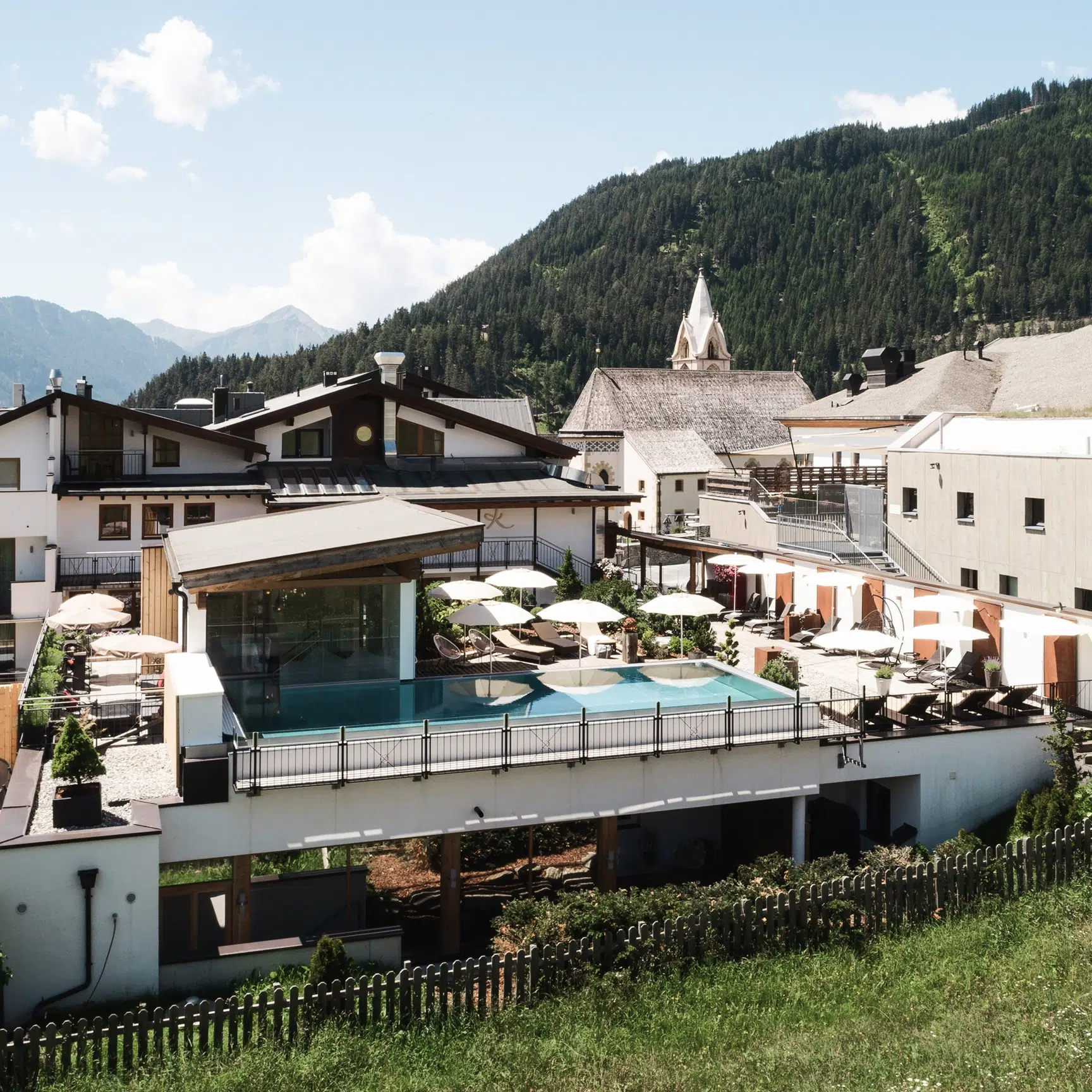 Modernes Hotel Das Köhle mit Pool auf dem Dach, Blick auf die Berge und traditionelle Gebäude an einem sonnigen Tag.