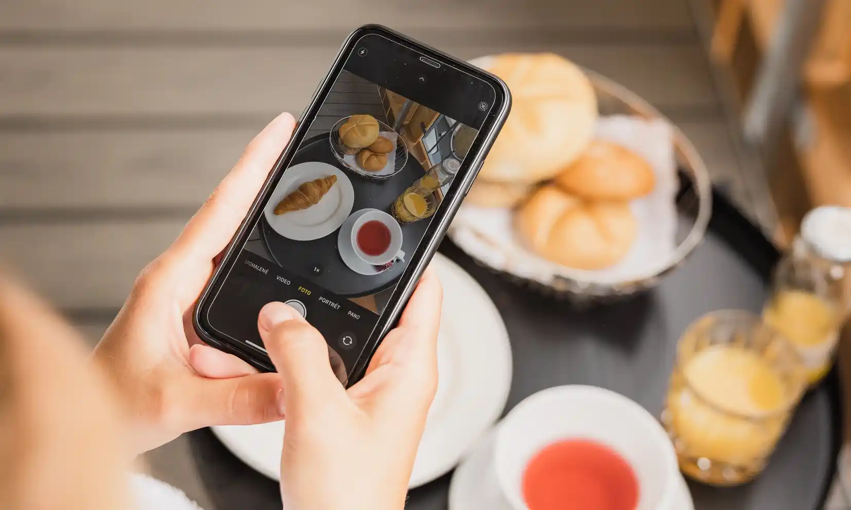 Eine Person genießt die Halbpension und fotografiert das Frühstück mit Croissants, Saft und Tee.
