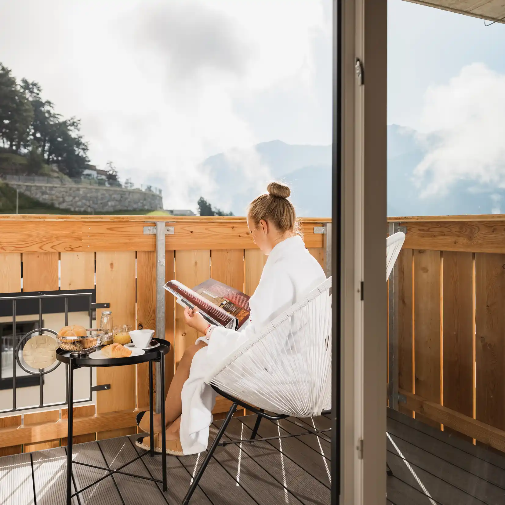 Frau im weißen Bademantel liest auf einem Balkon mit Frühstück, Bergblick und Köhles Spitzenteam.