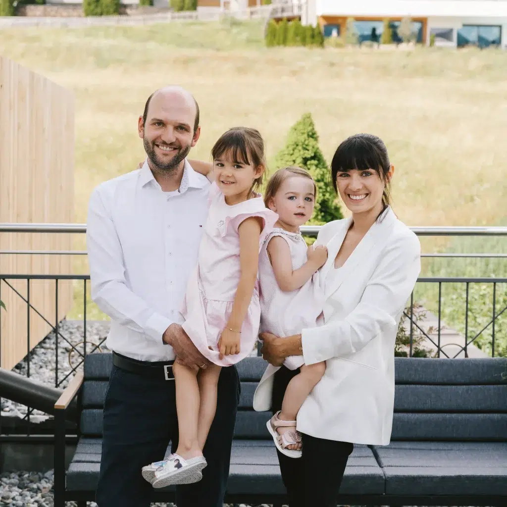 Eine vierköpfige Familie lächelt im Freien, während die Eltern von Köhles Spitzenteam ihre beiden kleinen Töchter im Arm halten.