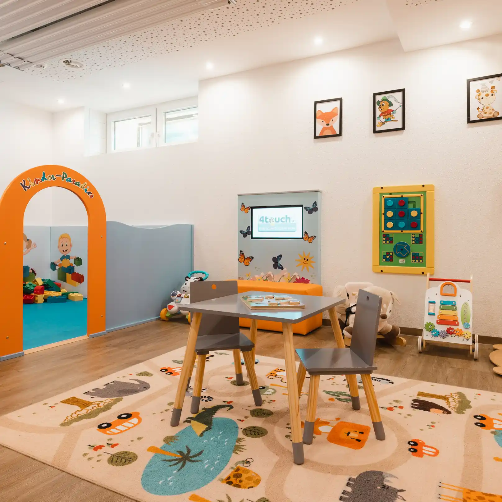 Helles, modernes Spielzimmer in einem Familienskigebiet mit Spielzeug, Kindertisch, Stühlen und Wandkunst.