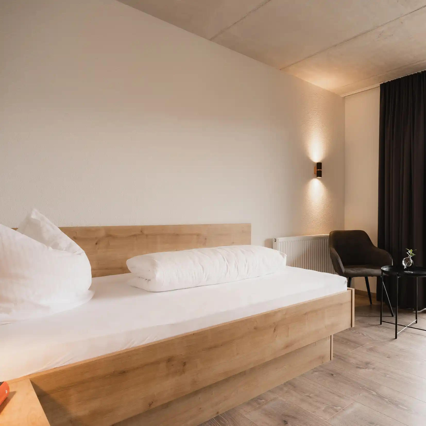 Minimalistisches Schlafzimmer von Köhles Spitzenteam mit einem Holzbett, weißem Bettzeug, Stuhl und Tisch.