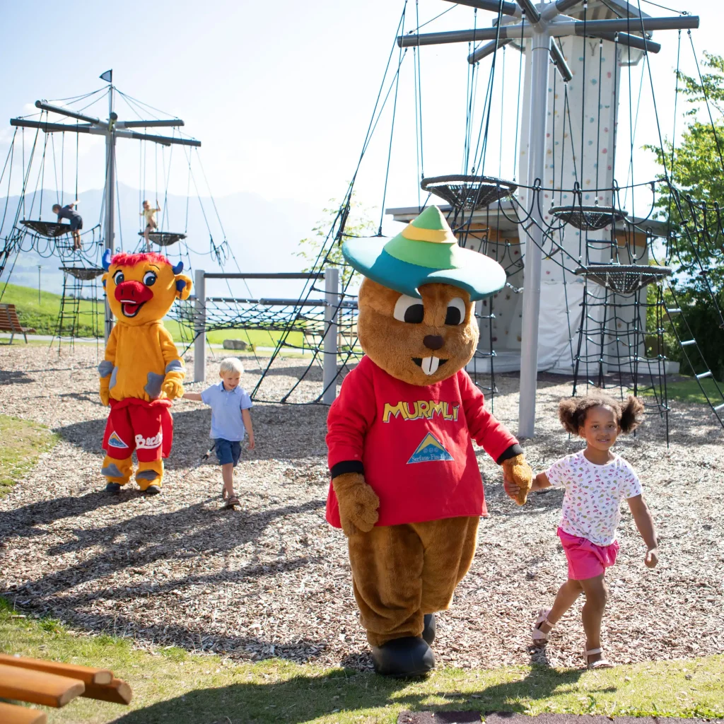 Zwei Kinder halten mit KidVenture-Bären auf einem Spielplatz im Freien Händchen.