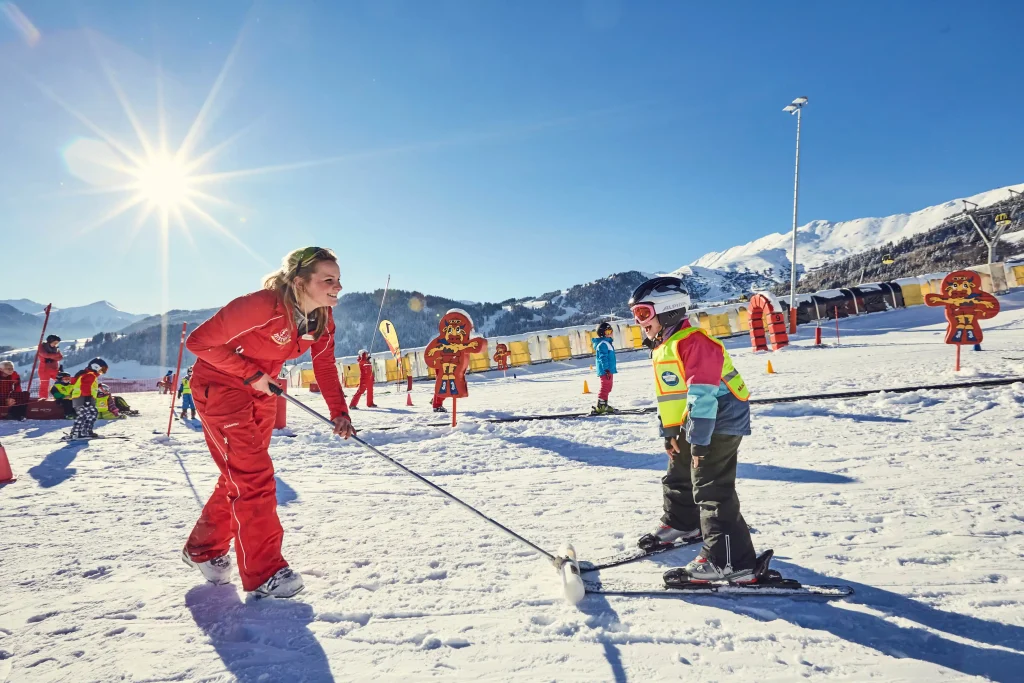 Skilehrer unterrichtet ein Kind auf einer sonnigen Piste in einem Familienskigebiet mit Bergblick.