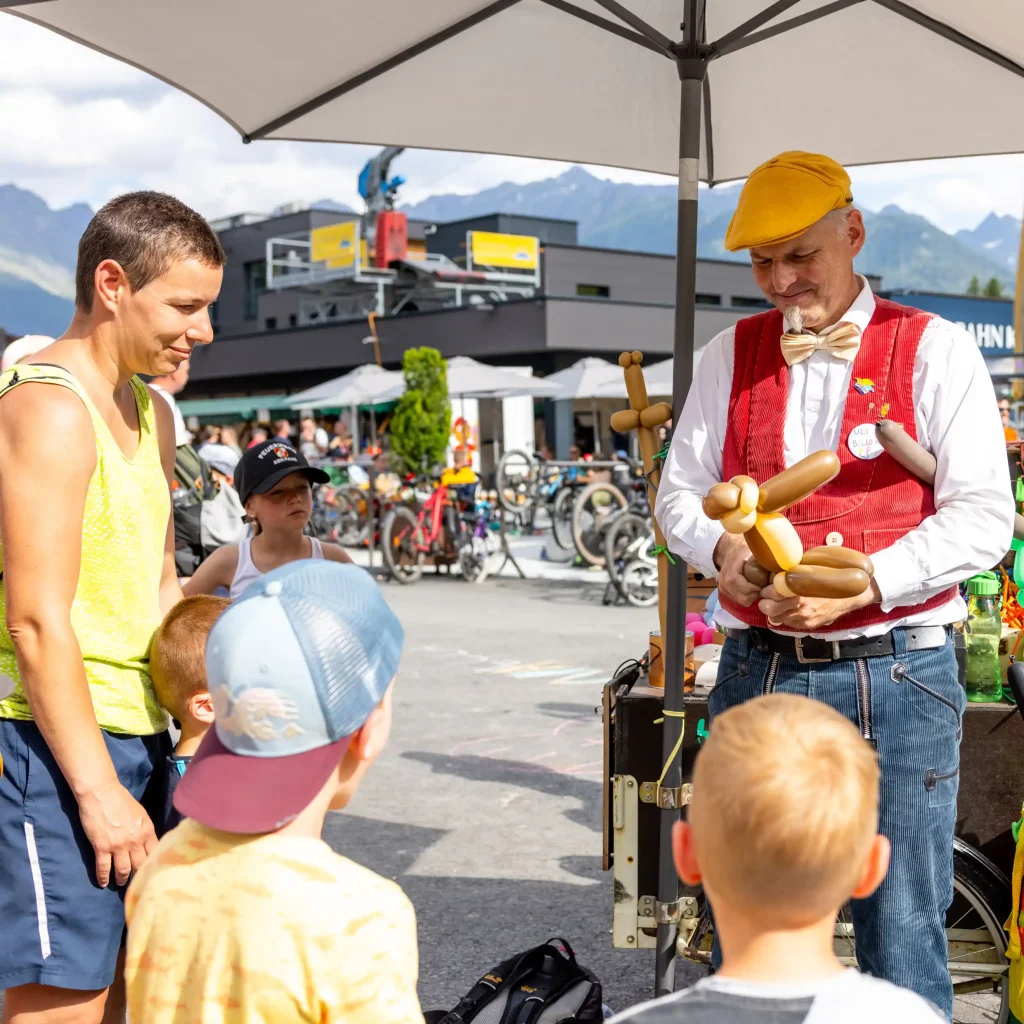 Ein Straßenkünstler macht Ballontiere für Kinder in der Nähe von Hügeln bei einer Veranstaltung im Freien.